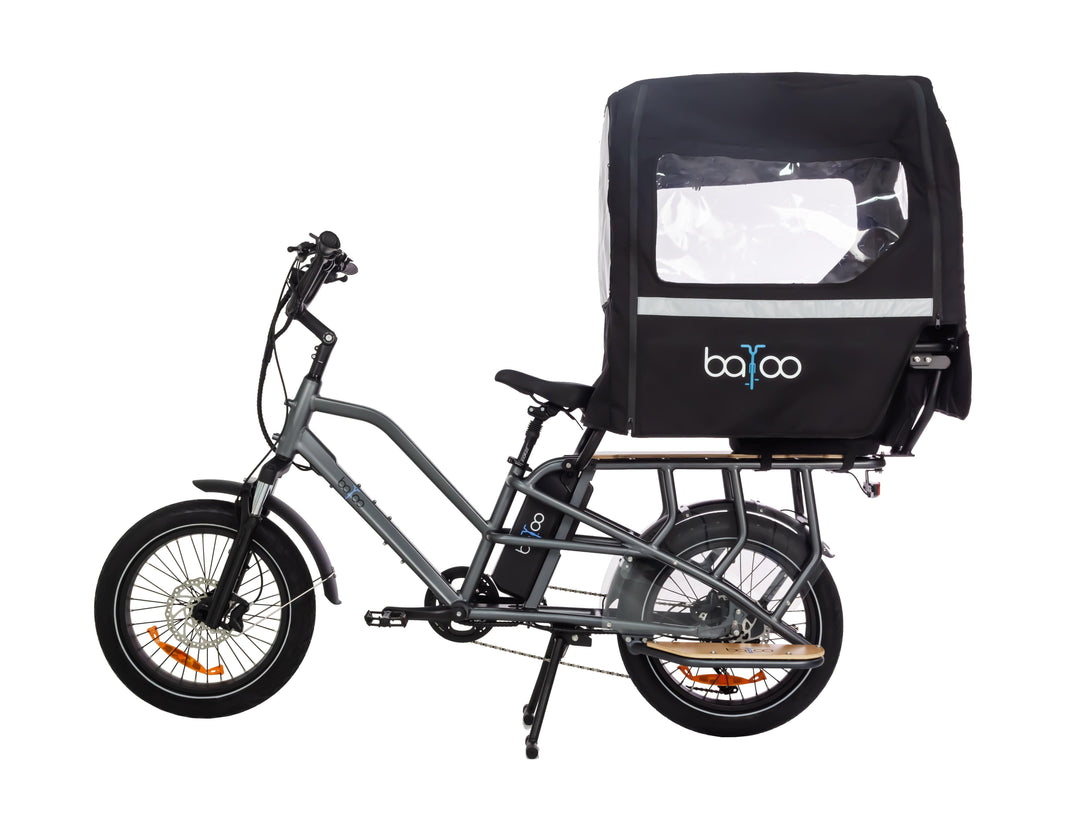 Vélo cargo électrique vu de profil, équipé d’une cabine de pluie pour enfants.