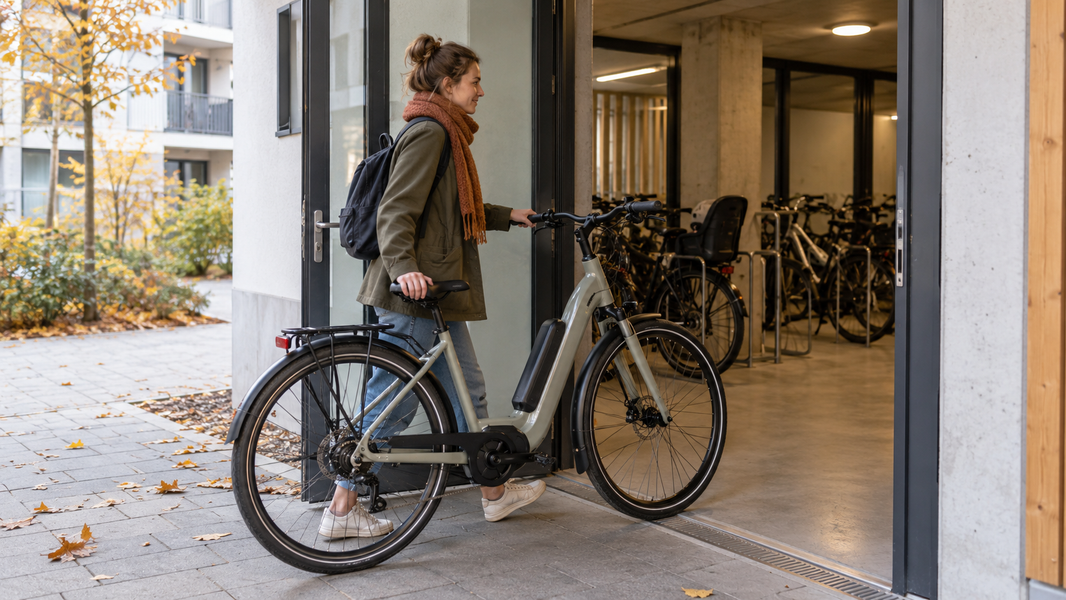 Une personne accompagne son vélo électrique dans le local à vélos d’un immeuble.