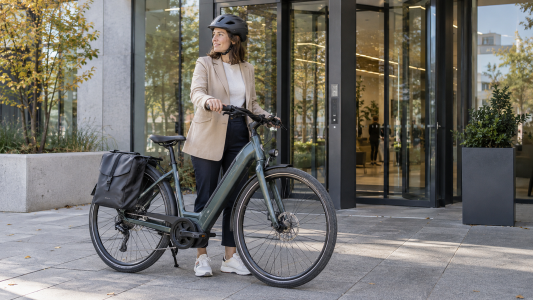 Une cycliste avec un vélo électrique devant l’entrée d’un bureau.